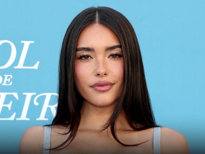 Madison Beer is seen posing for a photo in front of a blue wall. She's wearing a dress with light blue straps.