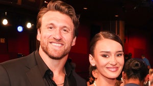 Kyle and Kristin Juszczyk are pictured at what appears to be a high-profile event. He's wearing a black jacket and a matching shirt, while she's wearing a white dress and several pieces of jewelry.