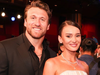 Kyle and Kristin Juszczyk are pictured at what appears to be a high-profile event. He's wearing a black jacket and a matching shirt, while she's wearing a white dress and several pieces of jewelry.