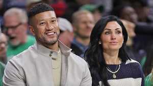Marcus and Joanna Freeman are sitting next to each other at what appears to be a sporting event. He's wearing a beige jacket and an off-white sweater, while she's wearing a blue-and-white striped pullover.