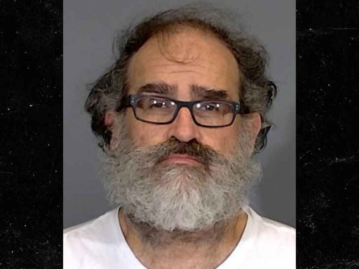 Michael Lewis is seen posing for a mugshot. He's wearing a white t-shirt and glasses.