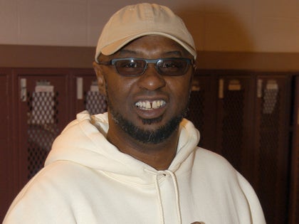 Joe Bryant Smiling While Wearing Glasses And A Beige Hat