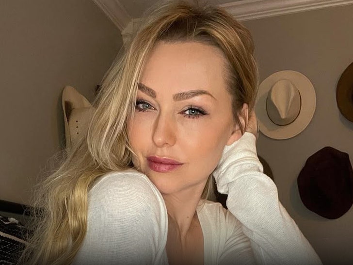 Leticia Cline is seen posing for a photo in front of a wall of hats. She's wearing a white long-sleeve top.