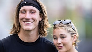 Trevor Lawrence is seen standing next to his wife Marissa. He's wearing a shirt with a graphic for the Jacksonville Jaguars, and she's got a pair of sunglasses perched just above her forehead.