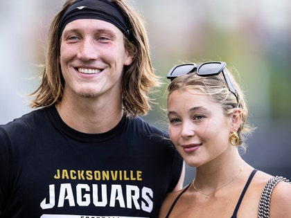 Trevor Lawrence is seen standing next to his wife Marissa. He's wearing a shirt with a graphic for the Jacksonville Jaguars, and she's got a pair of sunglasses perched just above her forehead.