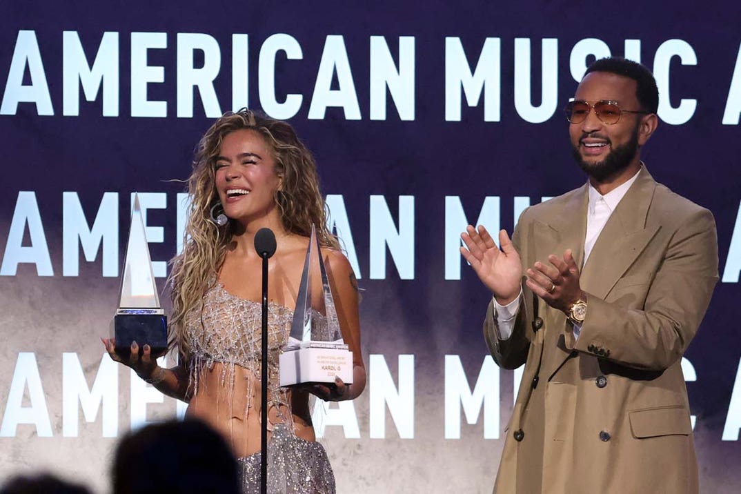 Karol G reacts as US singer-songwriter John Legend (R) presents her with the International Artist Award of Excellence and Best Latin Album for 