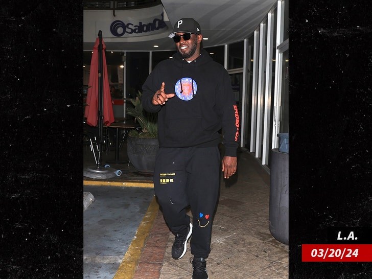 Diddy walking in a shopping plaza while wearing a black sweatpants, a black hoodie, and a black hat.