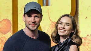 Liam Hemsworth and Gabriella Brooks are seen at a movie premiere. He's wearing a dark blue crewneck sweater and she's wearing a black dress.