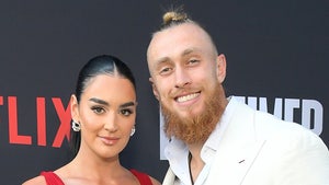 George Kittle is smiling while standing next to his wife, Claire, at an even for Netflix. He's wearing a cream-colored jacket and a white shirt, while she's wearing a red dress.