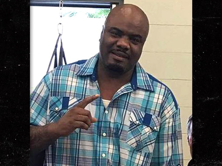 Quenton Marselles Brown is seen in what appears to be a gym. He's pointing his right index finger towards the ceiling, and he's wearing a blue plaid shirt.