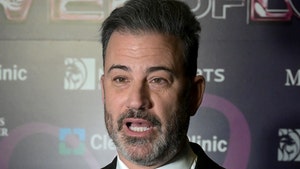 Jimmy Kimmel is seen at a red carpet event. He's wearing a black jacket, a matching tie, and a white button-up shirt.