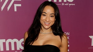 A woman wearing a black dress and silver necklace is standing in front of a burgundy wall featuring several logos.