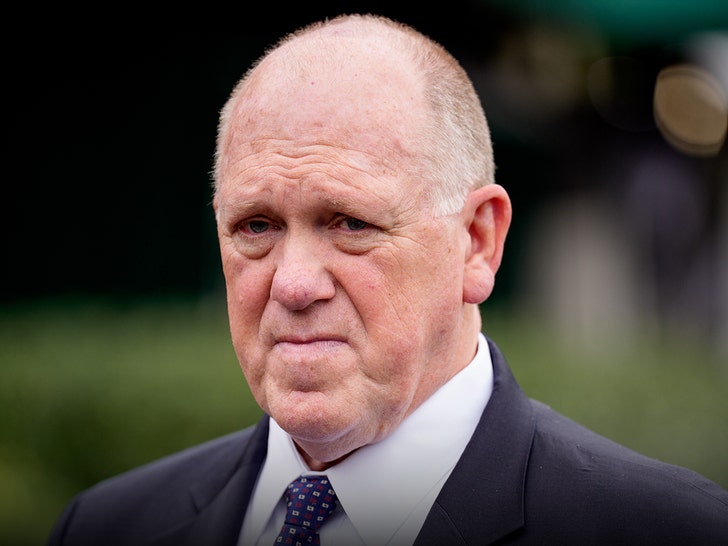 Tom Homan is seen at an outdoor event. He's wearing a black jacket, a white shirt, and a patterned tie.