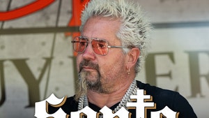 Guy Fieri's looking concerned behind the logo for Santo Tequila. He's wearing a black t-shirt, several chains, and orange-tinted aviator-style sunglasses.