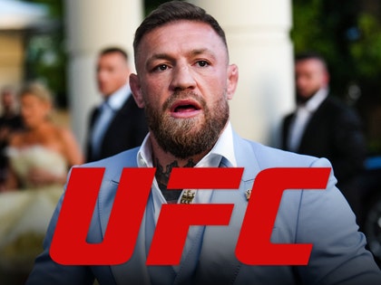 Conor McGregor is looking concerned behind the logo of the UFC. He's wearing a light blue jacket and a white button-up shirt.
