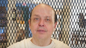 Robert Roberson is seen in a prison. He's wearing a white t-shirt underneath a white jumpsuit, and he has a small microphone attached to his chest.
