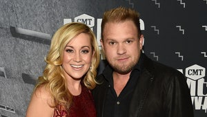 Kellie Pickler and Kyle Jacobs are seen at an awards show. She's wearing a red dress, while he's wearing a black button-up shirt and a matching jacket.