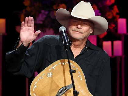 Alan Jackson's seen performing at a concert. He's wearing a black button-up shirt and a beige ten-gallon hat.