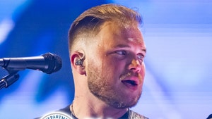 Zach Bryan's performing behind the logo for ICE. He's wearing a black t-shirt.