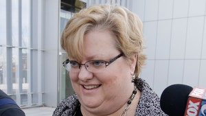 Kathryn Nester is seen while taking questions from reporters. She's wearing a patterned coat, a black blouse and a necklace.