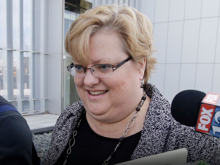 Kathryn Nester is seen while taking questions from reporters. She's wearing a patterned coat, a black blouse and a necklace.