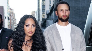 Ayesha Curry is seen walking next to her husband Stephen. She's wearing a patterned black dress, while he's wearing a white t-shirt and a gray cardigan sweater.
