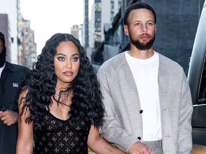 Ayesha Curry is seen walking next to her husband Stephen. She's wearing a patterned black dress, while he's wearing a white t-shirt and a gray cardigan sweater.