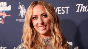 A woman wearing a sparkling silver dress is smiling while posing in front of a navy blue wall with several logos running across its surface.