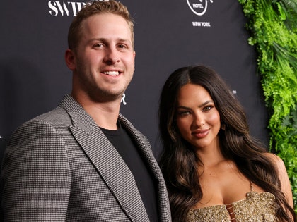 Jared Goff is seen standing next to his wife Christen. He's wearing a patterned jacket and black t-shirt, while she's wearing a gold-colored dress.