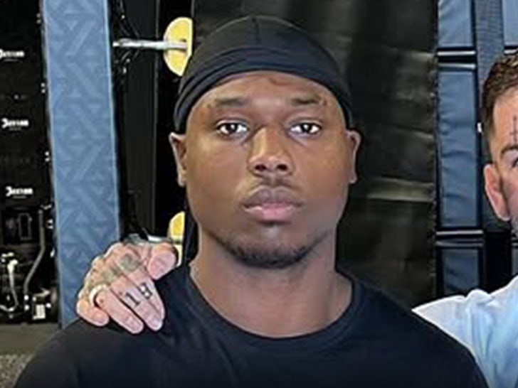 Raja Jackson's seen standing next to a friend in a gym. He's wearing a black t-shirt and a matching durag.