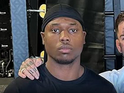 Raja Jackson's seen standing next to a friend in a gym. He's wearing a black t-shirt and a matching durag.