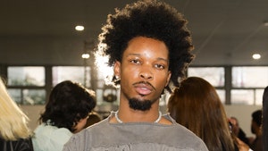 D4vd is seen posing for a photo at an event. He's wearing a distressed gray shirt and a necklace.