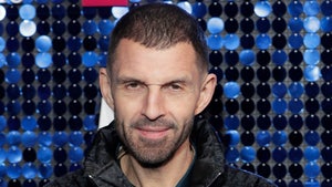 Tim Westwood is seen posing for a photo. He's wearing a black and patterned puffer jacket on top of a blue shirt.