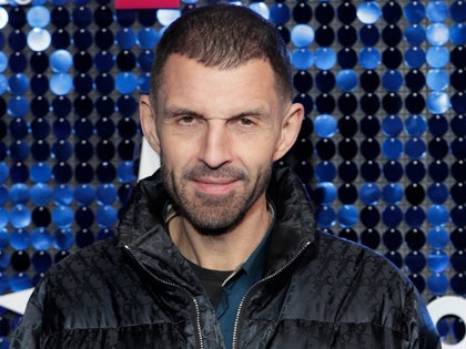 Tim Westwood is seen posing for a photo. He's wearing a black and patterned puffer jacket on top of a blue shirt.