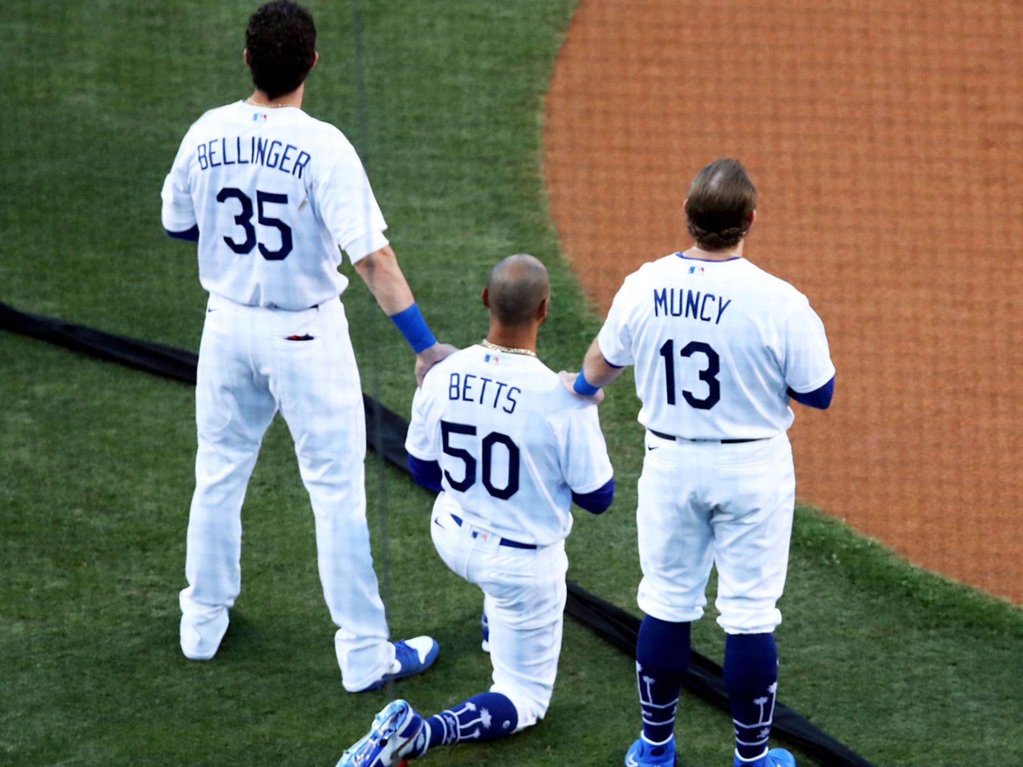 MLB - Mookie Betts takes a knee during the National Anthem, supported by  teammates Cody Bellinger and Max Muncy.