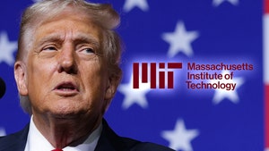 Trump is seen next to the logo for MIT. He's wearing a blue jacket, a white shirt, and a red tie.