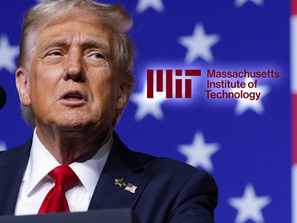 Trump is seen next to the logo for MIT. He's wearing a blue jacket, a white shirt, and a red tie.