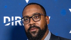 Marcus Jordan is pictured in front of a graphic for DirecTV. He's wearing a dark blue jacket on top of a light gray shirt.