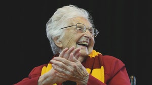 Sister Jean is seen clapping at a sports event. She's wearing a red long-sleeve shirt and a striped scarf.
