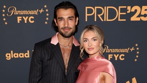 Sam Asghari and Brooke Irvine are seen at an event for Paramount+. He's wearing a striped jacket with a partially pink collar, and she's wearing a pink dress.