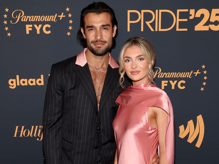 Sam Asghari and Brooke Irvine are seen at an event for Paramount+. He's wearing a striped jacket with a partially pink collar, and she's wearing a pink dress.