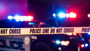 A pair of police cars with flashing red and blue lights are parked behind a line of police tape with text reading 