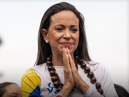 Maria Corina Machado is seen placing her hands together. She's wearing a multicolored t-shirt and several necklaces.