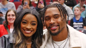 Simone Biles and her husband Jonathan Owens are smiling while sitting next to each other. She's wearing a leather jacket, and he's dressed in a white t-shirt underneath a white jacket.