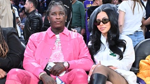 Mariah The Scientist and Young Thug are seen posing for a photo at a basketball game. He's wearing an all-pink outfit, while she's wearing a white blouse, fishnet leggings, leather boots and dark sunglasses.