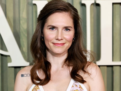 Amanda Knox is seen at what appears to be an awards show. She's wearing a multicolored dress, and her brunette hair is falling onto her shoulders.