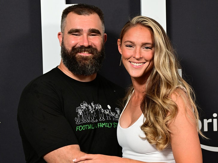 Jason and Kylie Kelce are hugging at an event for Amazon Prime. He's wearing a black t-shirt and she's dressed in a white tank top.