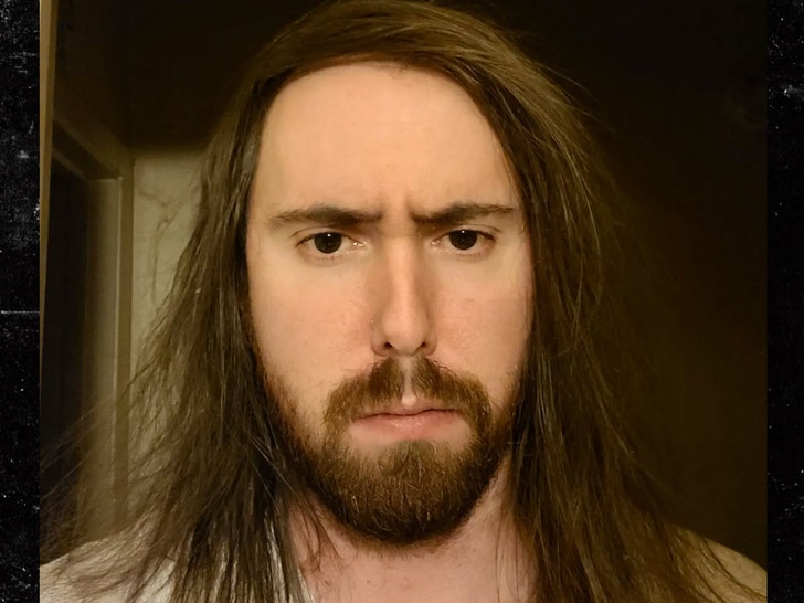 Twitch streamer Asmongold is seen frowning in a selfie. His long brunette hair's falling onto his shoulders.