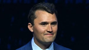 Charlie Kirk is seen while flashing a slight smile. He's wearing a dark blue jacket, a light blue shirt, and a red tie.